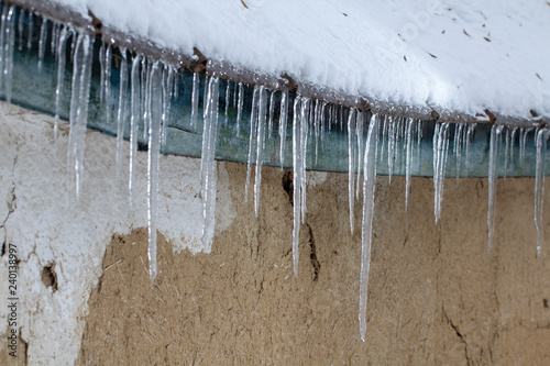 Icicles on an old  rusty  rural roof. Clay wall