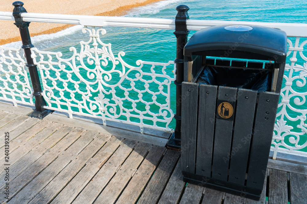 Naklejka premium Black wooden garbage on the seafront beach at the Brighton Pier for tourist and visitor. Save the ocean background concept.