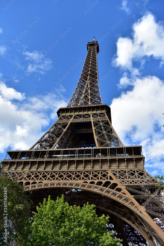 Eiffel Tower, perspective from below. Paris, France. Trees and blue sky with clouds.