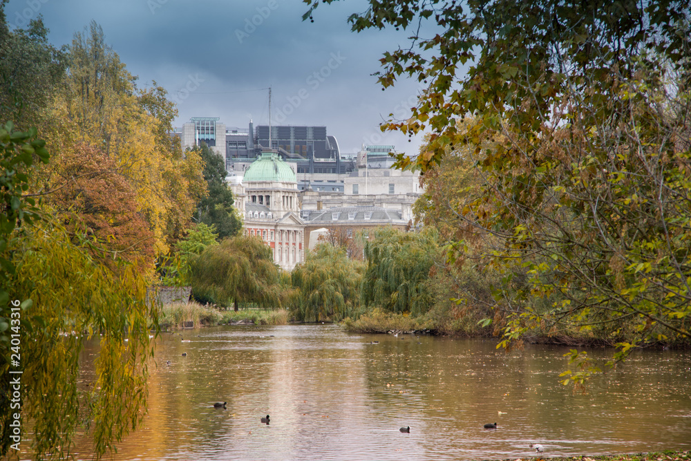 Landscape view of trees and lake in Hyde park with buildings in the background. Daylight, London, autumn in England.