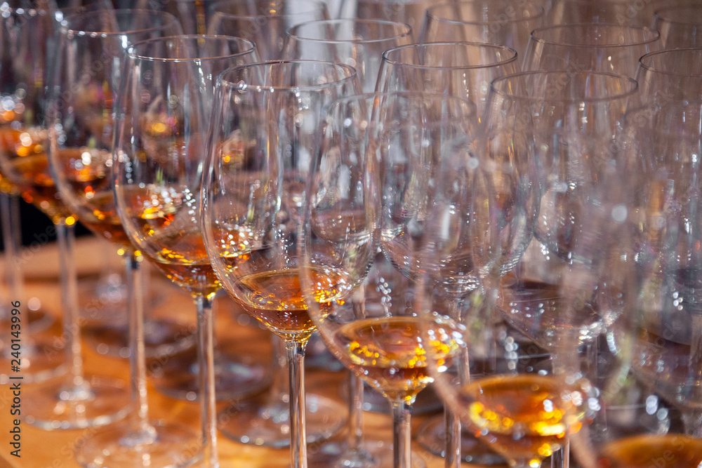 Closeup wine glasses with cognac stand in row on wooden shelves. Side view. Concept of degustation spirits: whiskey, brandy, porto, bitter, sherry on bartenders sommelier competition, exhibition Closeup wine glasses with cognac stand in row on wooden shelves. Side view. Concept of degustation spirits: whiskey, brandy, porto, bitter, sherry on bartenders sommelier competition, exhibition