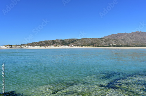 Beach with clear and turquoise water and small mountain. Sunny day, blue sky. Galicia, Spain.