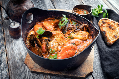 Traditional Catalan fish stew romesco de peix with prawns, mussels and fish as closeup in a modern design cast-iron roasting dish