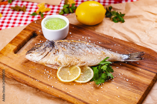 Grilled dorado fish with lemon and sauce on wooden board. Close up