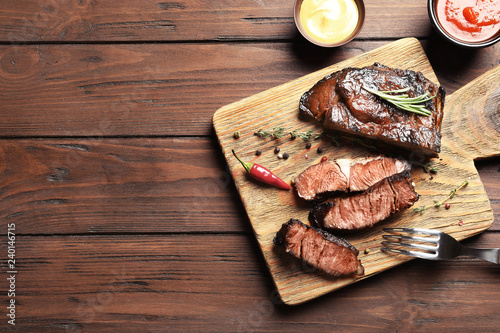Flat lay composition with delicious barbecued meat on wooden background. Space for text