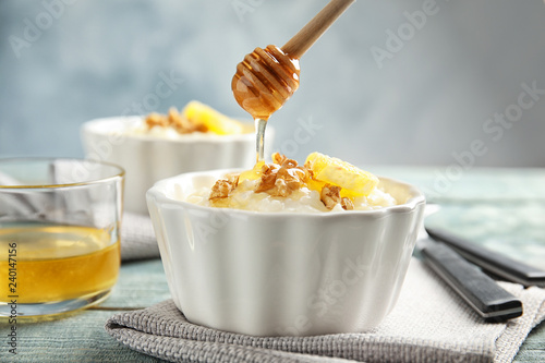 Pouring honey onto rice pudding with walnuts and orange slice in ramekin on table
