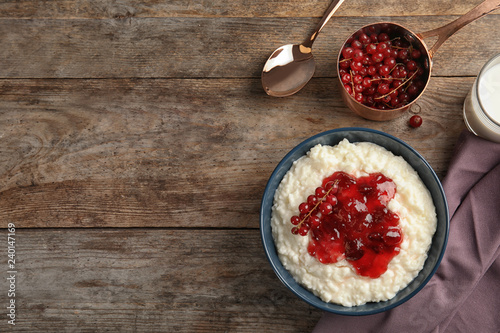Creamy rice pudding with red currant and jam in bowl served on wooden table, top view. Space for text
