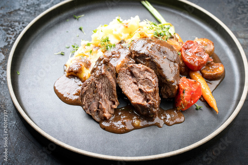 Traditionelle deutsche geschmorte Schweinebäckchen in brauner Rotwein Sauce mit Pilzen und Kartoffelpüree als closeup auf einem Modern Design Teller