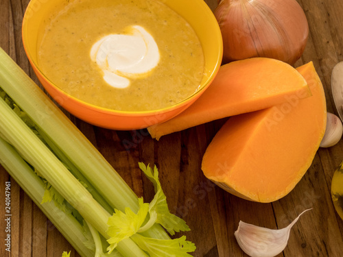 Pumpkin and carrot soup with cream on dark wooden table with selery, garlick and  pieces of pumpkin