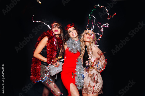 Birthday party, new year carnival. Young smiling women on white background celebrating brightful event, wears elegant fashion dresses and yellow crown. Sparkling confetti, having fun, dancing