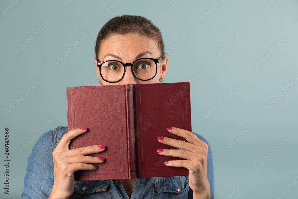 beautiful young girl in glasses holding a book with astonishment on her face on a blue background beautiful young girl in glasses holding a book with astonishment on her face on a blue background