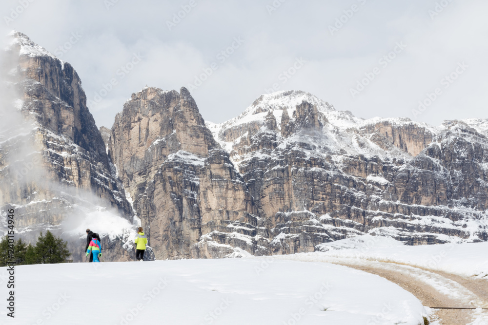 Pralongià, Italy - August 25, 2018: people stroll in alpine scenery with snow-covered meadows along a road
