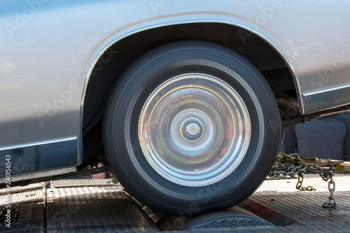 A car running at full speed on a dynamometer. The car is not moving but the wheel is spinning full speed. Closeup side view, in the shadows outdoors. © madscinbca