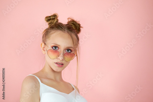 Portrait pretty young woman in pink sunglasses shape of heart. girl with a funny hairstyle on a bright background