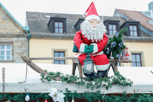 Weihnachtsmann mit grünen Handschuhen und Licht in der hand auf einem Schlitten der mit Tannenbaumästen geschmückt ist auf dem Christkindlmarkt in Bayreuth. photo