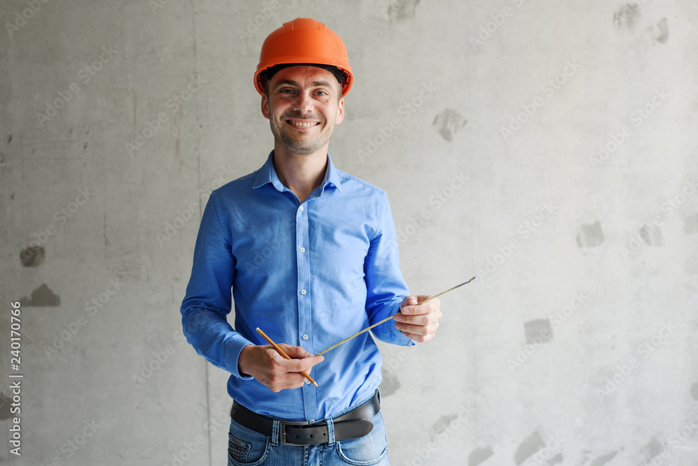 Satisfied construction worker foreman measures a tape measure of a wall parameter in a house under construction. Inspects repair readiness and accuracy of work performed Satisfied construction worker foreman measures a tape measure of a wall parameter in a house under construction. Inspects repair readiness and accuracy of work performed
