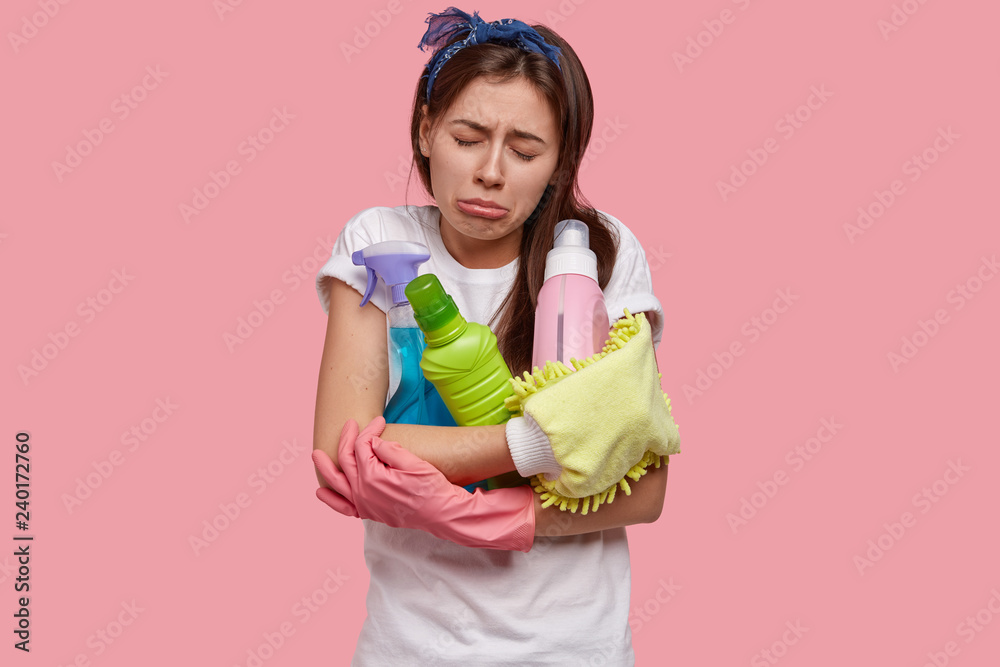 Crying disappointed tired young woman feels unhappy after spring cleaning, holds all necessary supplies, detergents, has miserable facial expression, being in low spirit, fatigue from washing