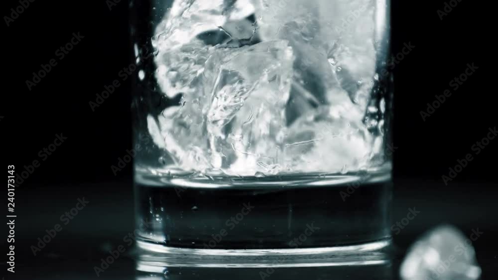 Crystal ice falling in glass on dark background. Close up slow motion footage. Crystal ice falling in glass on dark background. Close up slow motion footage.