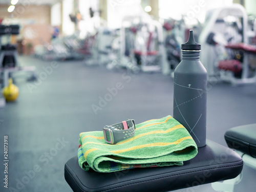 Canvas Print closeup of a water bottle and sport watch on a gym bench with threadmills and training machines blurred on background