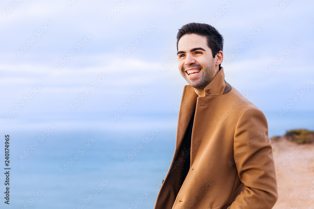 The guy holds his hands in the pockets of a beige coat and laugh The guy holds his hands in the pockets of a beige coat and laugh