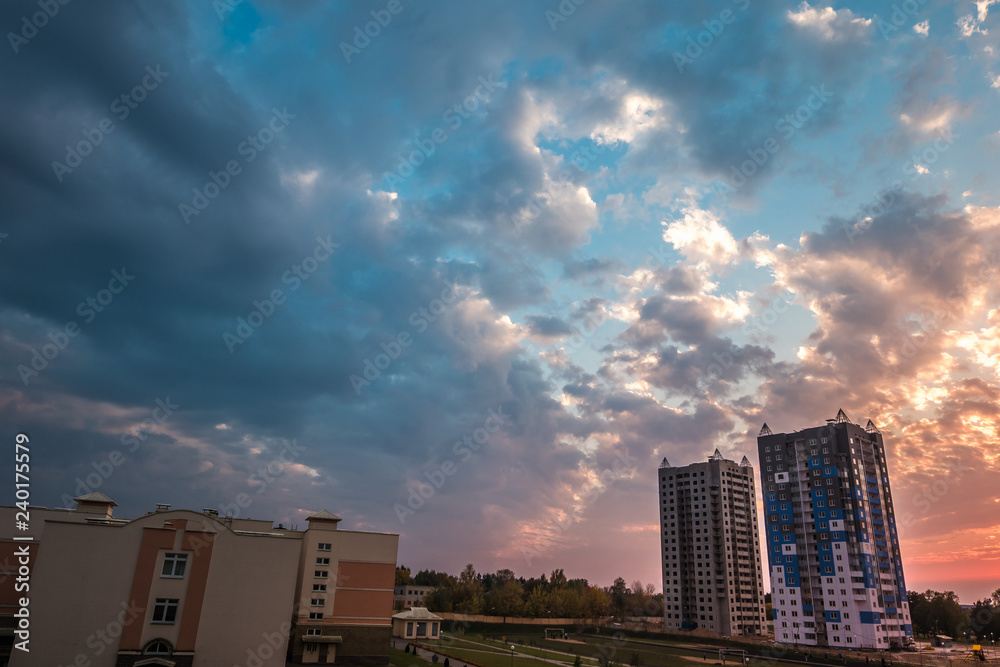 Fototapeta premium evening fluffy curly rolling clouds of awesome sunset against the background of multi-storey apartment buildings