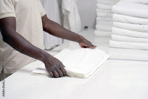 Hands of an african male laundry hotel worker folds a clean white towel. Hotel staff workers. Hotel linen cleaning services.