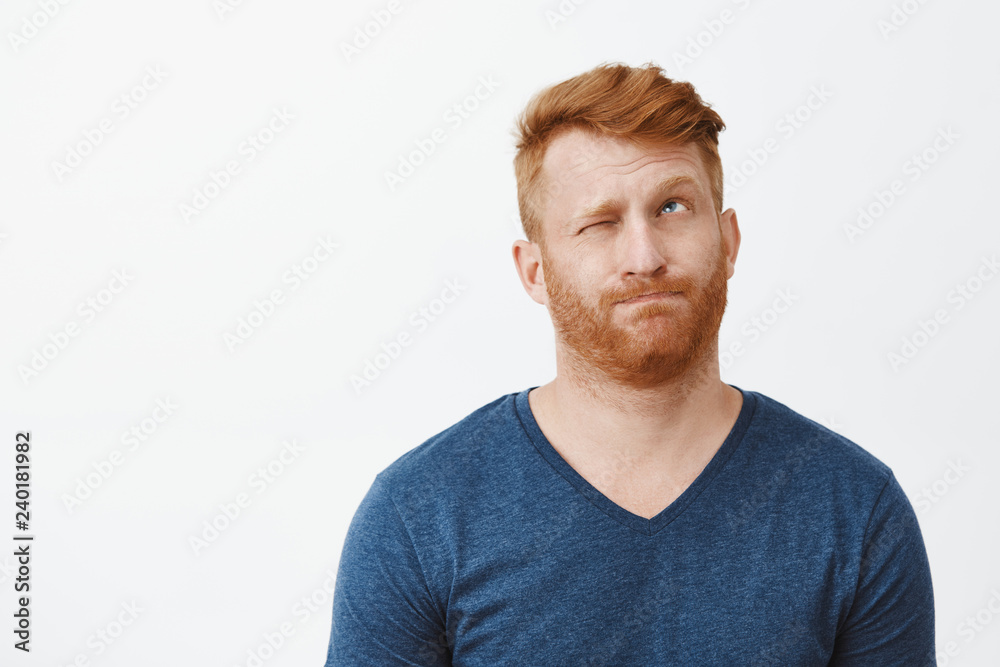 Redhead attractive male with bristle in casual blue t-shirt, pursing lips making hmm sound, closing one eye and looking up, thinking or making decision, trying calculate in mind or make up idea Redhead attractive male with bristle in casual blue t-shirt, pursing lips making hmm sound, closing one eye and looking up, thinking or making decision, trying calculate in mind or make up idea