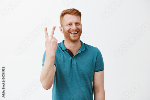 Showing you two steps to successful business. Portrait of friendly-looking happy and joyful redhead male with beard making sign twice and smiling broadly while standing over gray background photo