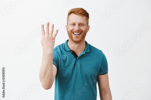 Indoor shot of pleased and satisfied male redhead client with bristle in green polo shirt showing number four with fingers and smiling broadly, being pleased with good fourth place over grey wall