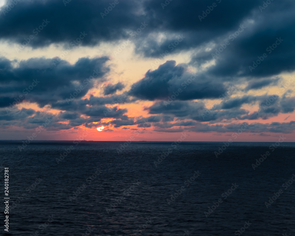 Beautiful Caribbean sunset with purple and red tones. Cloudy evening sky over the ocean in a tranquil warm scene.