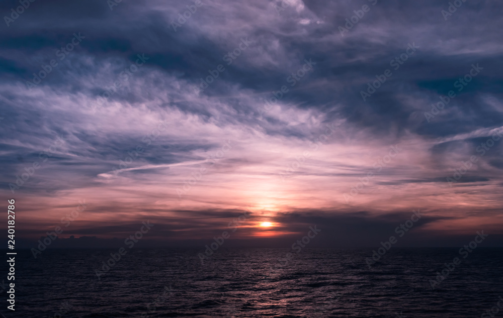 Beautiful dark blue and purple sunset with soft clouds over the ocean. Light of the setting sun reflected on the surface of the calm Caribbean Sea.