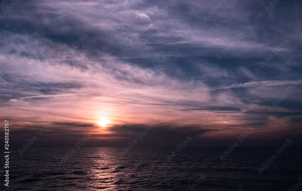 Incredible purple and blue sunset over the Caribbean Sea. Sunlight reflected on the water from the dramatic sky. The coastline of Cuba in the distance on the horizon.