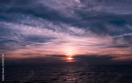 Beautiful dark blue and purple sunset with soft clouds over the ocean. Light of the setting sun reflected on the surface of the calm Caribbean Sea.