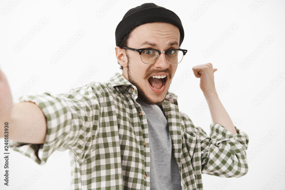 Man wanting save moment of triumph and victory yelling from joy and happiness pulling hand towards camera to take selfie during happy moment celebrating with raised fist over white background Man wanting save moment of triumph and victory yelling from joy and happiness pulling hand towards camera to take selfie during happy moment celebrating with raised fist over white background