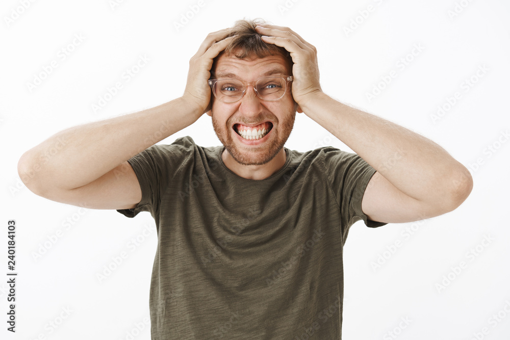 Troubled and perplexed guy needs vacation. Portrait of distressed annoyed young male office worker in green t-shirt and glasses clenching teeth holding hands on head in hopeless pose having crappy day Troubled and perplexed guy needs vacation. Portrait of distressed annoyed young male office worker in green t-shirt and glasses clenching teeth holding hands on head in hopeless pose having crappy day