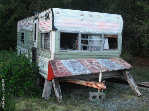 Abandoned camping trailer left behind in the deep woods on Vancouver Island in British Columbia. The interior is messy, windows are missing and nobody is living inside or using it for any purpose.
