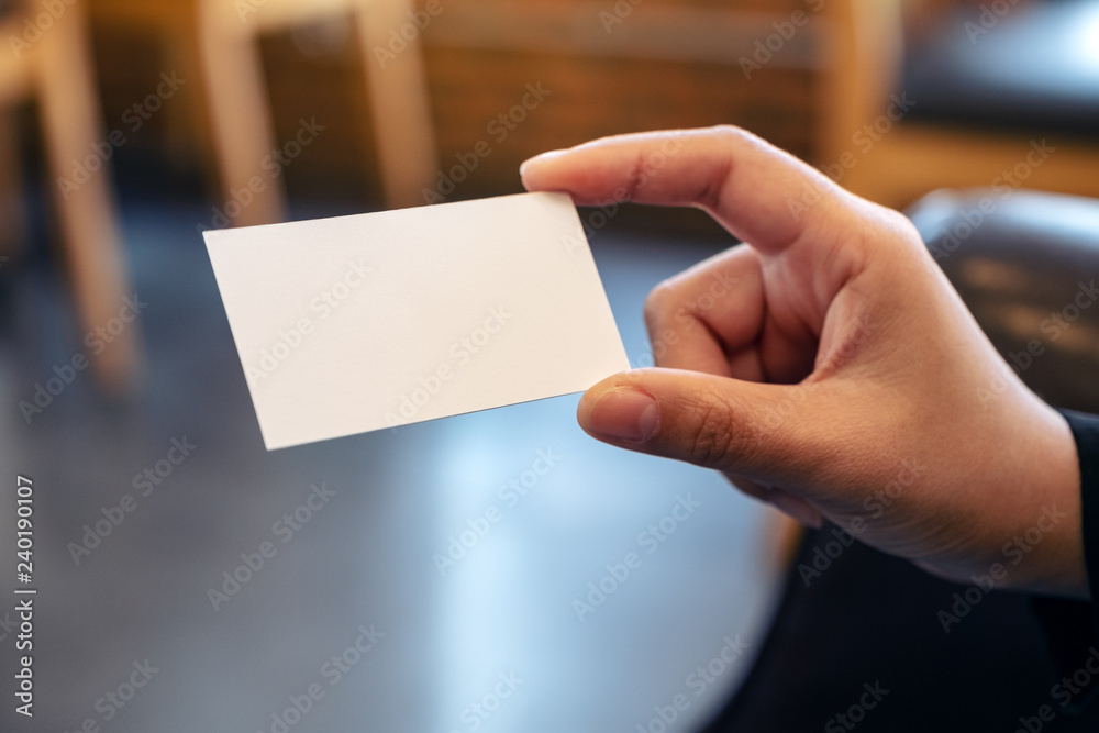 A hand holding white empty business card with blurred background A hand holding white empty business card with blurred background