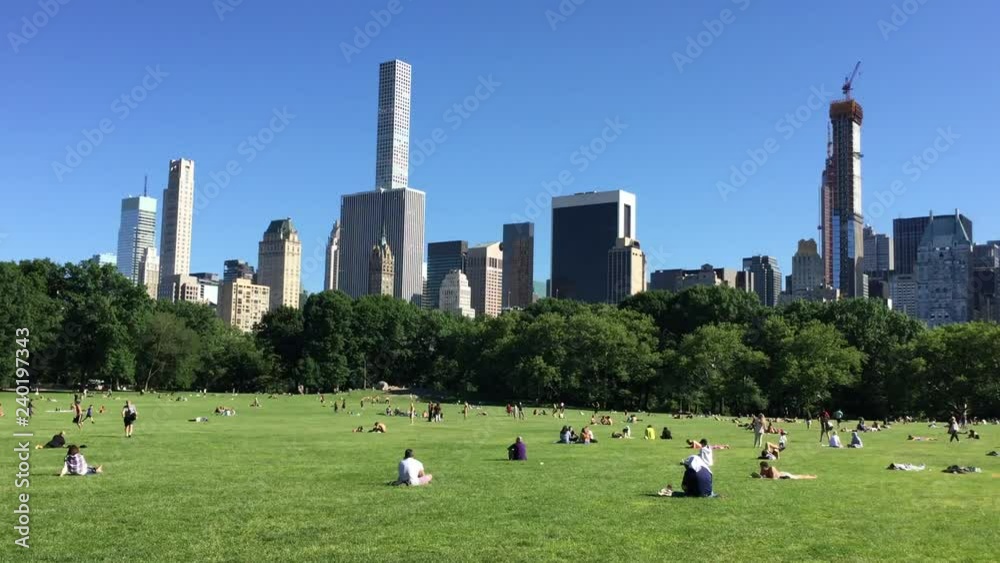 NEW YORK - JUNE 12, 2018: People in Sheep Meadown Central park on sunny day in Manhattan with buildings in background.