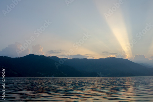 pink white lines of sunset sunlight in the blue sky above the silhouettes of the mountains and the lake