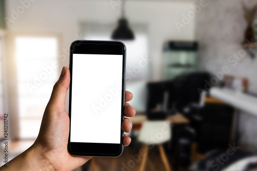 Hand held black phone With a blank white screen in the office in the morning light.