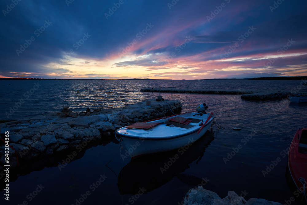 Beautiful summer seascape at sunset. Small boats anchored in sea inlet calm shallow water lit by red sun rays of setting sun. Tourism, fishing, diving, recreation and beauty of nature concept.