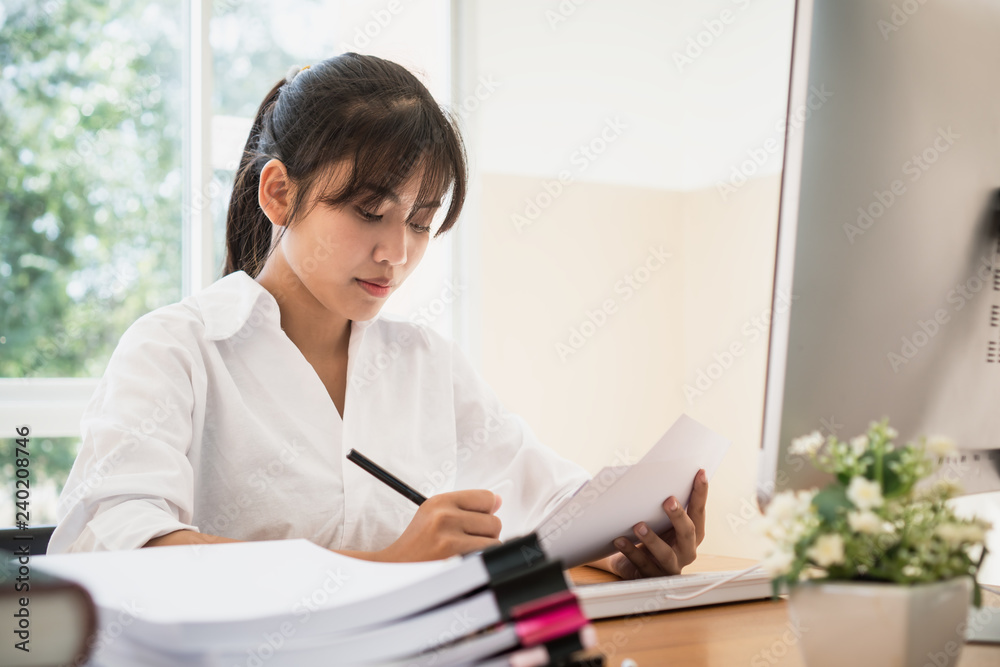 Asian Business woman offices check working for stack of unfinishedd documents papers on computer in busy office. Ideas for seaching paperwork and Accounting planning budget Annual report file concept Asian Business woman offices check working for stack of unfinishedd documents papers on computer in busy office. Ideas for seaching paperwork and Accounting planning budget Annual report file concept