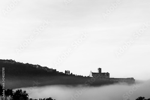A view of a silhouette of St.Francis church in Assisi in the middle of mist beneath a deep sky with clouds