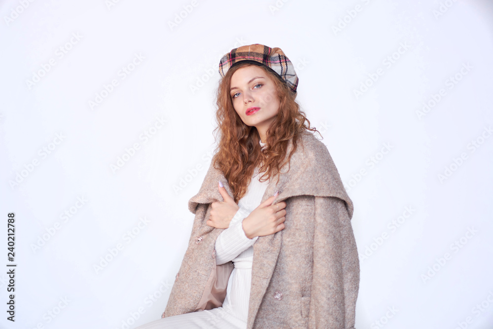 Beautiful girl dressed in french style on a white background. red hair woman is wrapped in a coat, winter clothes. Smiling lady wearing warm clothes, winter portrait