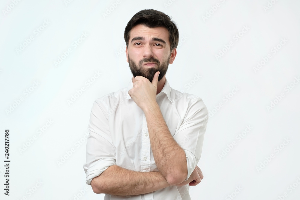 Portrait of a pensive spanish man in white shirt against a white background. He is trying to make a decision. Portrait of a pensive spanish man in white shirt against a white background. He is trying to make a decision.