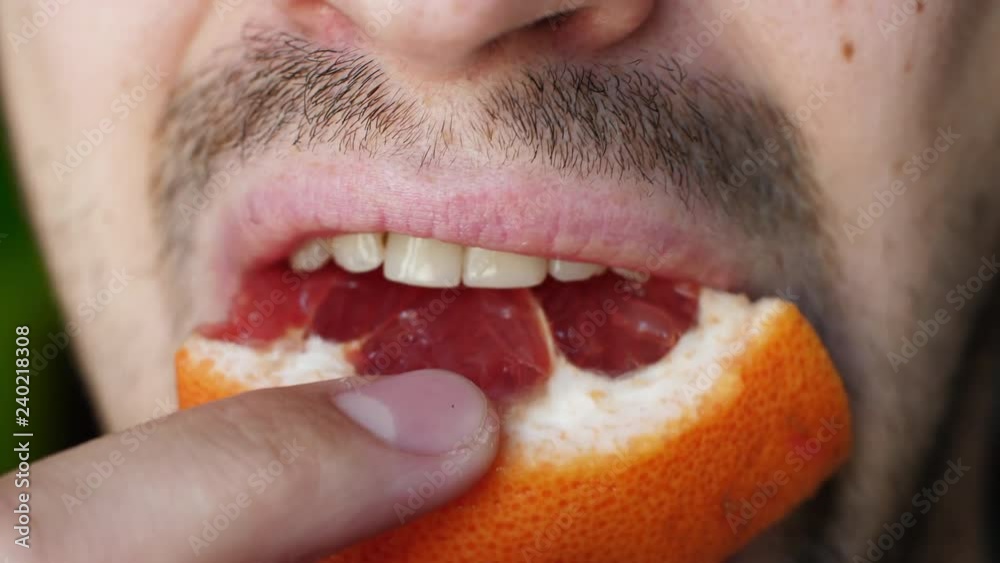 Close of unshaven man biting off and chewing slice of grapefruit. Male mouth chewing grapefruit