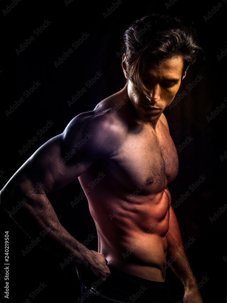 Handsome muscular shirtless young man standing confident, front view, looking away