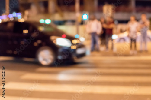 Abstract urban blurred background. Night view of the modern city street with moving vehicles, lighted and walking people.