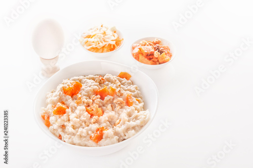 Oatmeal with pumpkin and nuts in a plate, vegetable salads and boiled egg on a white background. Close-up. Copy space