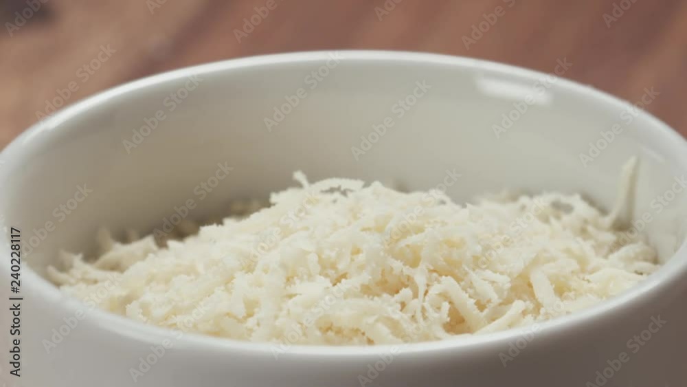 Slow motion closeup of grating aged parmesan in white bowl on wood table Slow motion closeup of grating aged parmesan in white bowl on wood table